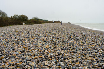Rocky shoreline at a grey and overcast day with visitors exploring the pebble beach