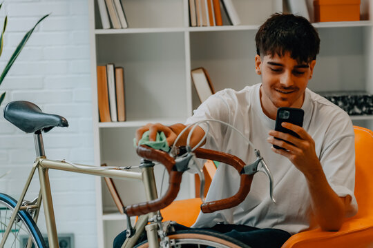 young man cleaning or preparing vintage bicycle looking at mobile phone or app