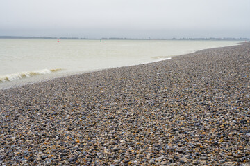 Coastal shoreline with pebbles and gentle waves under an overcast sky at dawn