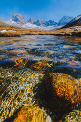 In the distance, there is an icy lake in front of majestic snow-capped mountains, with clear and transparent water flowing through it. Made by AI.