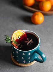 Mulled wine with orange, cinnamon and rosemary in a cup on a dark background with tangerines.