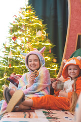 Christmas, New Year's photo. The children of a girl dressed as a unicorn and a fox cub are sitting on the couch, smiling, drinking milk and eating cookies.