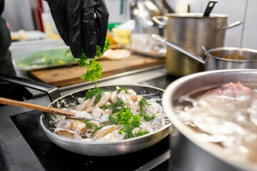 A chef garnishes a dish with fresh parsley in a modern kitchen. The pan is filled with creamy seafood, showcasing culinary skill and fresh ingredients. Perfect for food-related content.