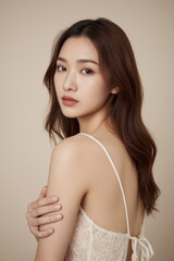 Fototapeta premium Photograph of a young Asian woman with long brown hair, wearing white lace lingerie, against a beige background.