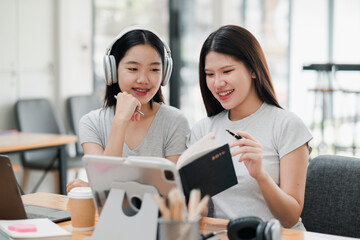 Two young women engaged in a collaborative work session, using a tablet and notebook in a modern office environment.