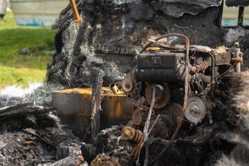 A burnt out engine in a boat wreck with ashes around = side view