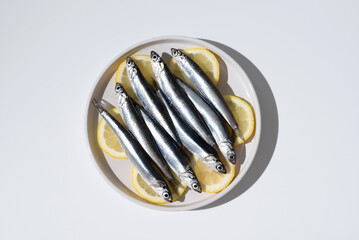Anchoas frescas sobre rodajas de limón dentro de un plato sobre fondo blanco. Vista superior