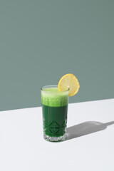 Jugo batido de espinacas adornado con una rodaja de limón sobre una mesa blanca y fondo verde