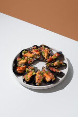 Plato de mejillones al vapor rellenos con vinagreta de tomate, pimiento rojo, pimiento verde y cebolla sobre una mesa blanca y fondo naranja