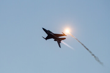  F-16 Jet Deploying Flares at Sunset. A Polish Air Force F-16 jet releases a glowing flare during an impressive aerial display against a twilight sky at the Leszno air show in Poland.