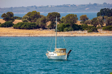Anchored by the Island Shore. A quaint sailboat anchored in turquoise waters near a rocky island...