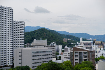 Malerischer Blick auf eine japanische Stadt mit Bergen im Hintergrund, umgeben von üppigem Wald, ruhige Landschaftmage