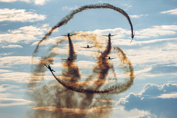 Eye-level view of a group of six airplanes performing an aerial maneuver, leaving trails of dark...