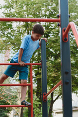 Happy boy playing and hanging on steel bar on playground. Children's exercises for health and concentration.