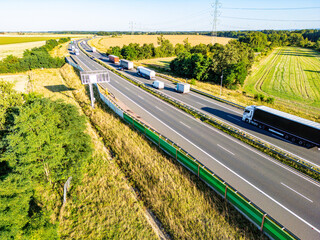 Busy A4 Highway in Rural Poland.  An aerial view of Poland's A4 highway bustling with trucks and cars, flanked by golden fields and lush greenery under a sunny sky.
