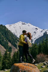 A young couple stands on a cliff and hugs each other against the background of the snowy peaks of the mountains. A man and a woman in love kiss in the mountains