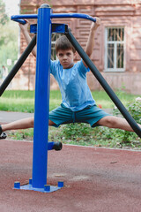 Obraz premium Happy boy doing sports on exercise machines on a summer playground. Children's exercises for health and concentration.
