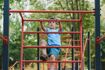 Happy boy playing and hanging on steel bar on playground. Children's exercises for health and concentration.