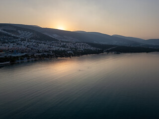 Twilight Reflections on Coastal Town. A serene coastal town basks in the golden twilight as the sun dips behind the hills, casting gentle reflections over the rippling waters.