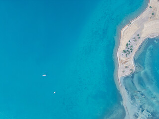Aerial Serenity Over Turquoise Waters. A stunning top-down aerial view of clear turquoise waters surrounding a small sandy shoreline, with two boats floating peacefully in the sea.