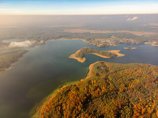 Obraz premium Golden Autumn Aerial Panorama. A mesmerizing aerial view of a lake surrounded by golden autumn foliage, misty clouds, and a charming village nestled by the water.