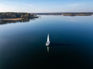 Sailboat on Tranquil Lake Waters. A serene aerial view of a white sailboat gliding across calm blue...