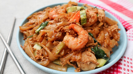 Kwetiaw or Kwetiau seafood, fried rice noodles with prawn or shrimp and vegetables. Popular in Indonesia served on blue plate isolated on grey. close up
