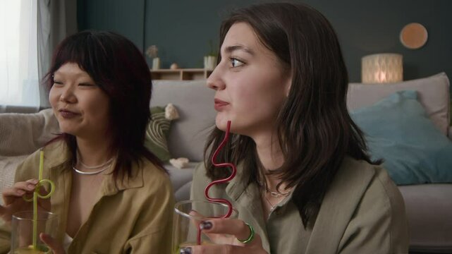 Handheld shot of positive female zoomers having refreshing non-alcoholic drinks while partying together at home