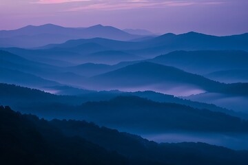 Fototapeta premium Layers of blue mountains at sunrise, shrouded in mist. A tranquil, scenic vista with soft light and a peaceful atmosphere. Deep blues and purples dominate the palette.