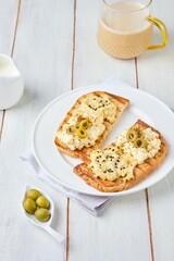 Healthy breakfast, two open sandwiches with hummus, egg salad and olives on white plate on light wooden background. Healthy food.