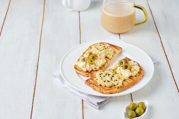 Healthy breakfast, two open sandwiches with hummus, egg salad and olives on white plate on light...
