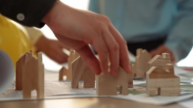 Architect and engineer discuss about building blueprint on table with architectural document, measurement tools scatter around at office, use wooden block for house positioning. Closeup. Delineation.