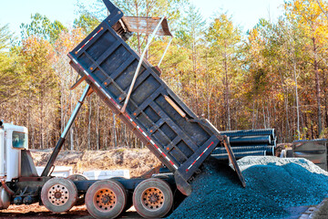Dump truck discharges gravel onto ground at construction site, during construction