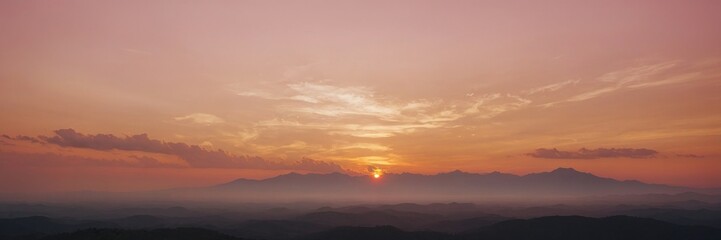 a breathtaking sunset painting the sky with warm hues, casting a golden glow over distant mountains and creating a tranquil atmosphere. The sun peeks through the clouds. wallpaper banner background