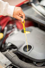 Hand checking oil level with dipstick in car engine compartment