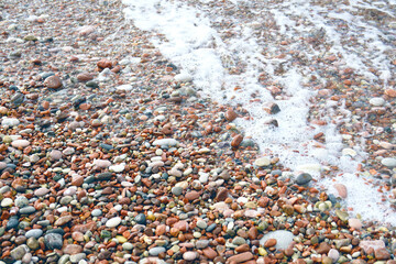 Summer background from the Mediterranean coast: a close-up of the pink pebble beach in Sveti Stefan, Montenegro. Bright stones of different colors and foam of the sea surf. Details from the seashore