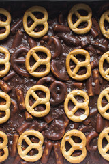 Overhead view of chocolate pretzel cookie fudge in a baking tin, Top view of cookie fudge in a parchment lined baking pan, process of making chocolate pretzel fudge