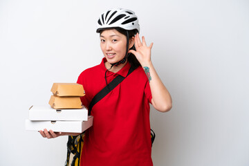 Young Chinese delivery woman taking takeaway food isolated on white background listening to something by putting hand on the ear