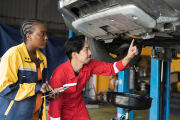 Male and female mechanic maintenance car engine at garage. Group of mechanics repairing car engine...