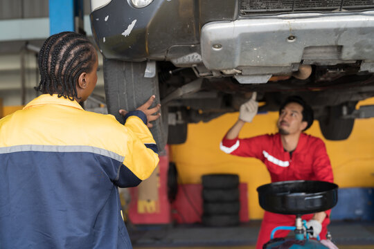 Female mechanic working at garage. Female mechanics checking tire wheel underneath lifted car at auto car repair service. Car service and Maintenance concept