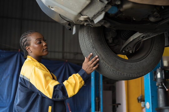 Female mechanic working at garage. Female mechanics checking tire wheel underneath lifted car at auto car repair service. Car service and Maintenance concept