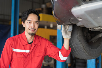 Male mechanic maintenance car engine at garage. Asian male mechanics repairing car engine underneath lifted car at auto car repair service