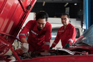 Group of Asian male mechanic maintenance engine car at auto repair shop. Male technician repairing engine car under hood of car in garage