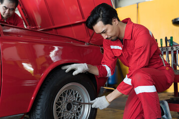 Male mechanic using pneumatic wrench changing tyre of car at auto repair shop. Mechanic checking, repair and maintenance wheel of car. Auto car repair service and maintenance concept