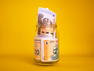 Zimbabwean gold zig notes in transparent glass jar bottle container isolated yellow background. savings concept
