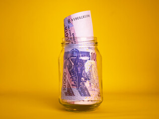 West African CFA franc notes in transparent glass jar bottle container isolated yellow background. savings concept
