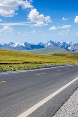 Countryside asphalt road and green meadow with mountains nature landscape on a sunny day. Outdoor natural background.