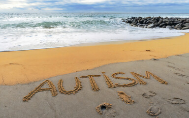 Fototapeta premium Autism word written on beach sand with child footprints. Awareness day concept.