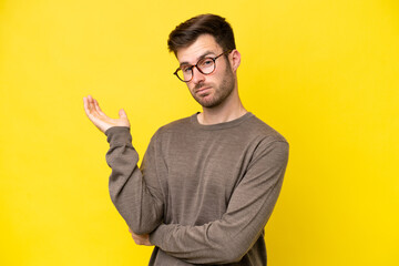 Young caucasian man isolated on yellow background having doubts