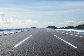 Straight asphalt road and island with sky clouds scenery under blue sky. Outdoor road background.